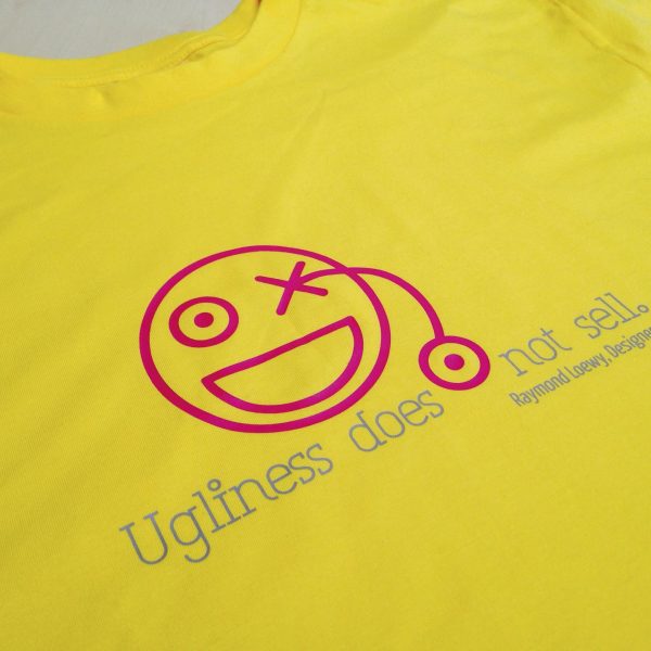 Gelbes T-Shirt mit pinkem Smiley und dem Zitat „Ugliness does not sell. – Raymond Loewy, Designer“ in blauer Schrift.