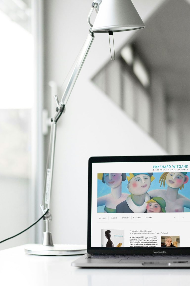 Silberne Schreibtischlampe neben einem Laptop mit einer Kunst-Website von Ekkehard Wiegand.