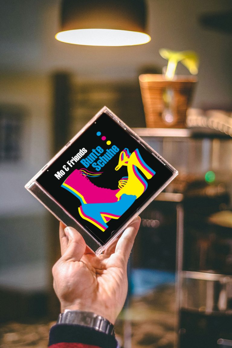 Hand hält eine CD mit dem Titel "Bunte Schuhe" und einem Keith Haring-ähnlichen Schuhmotiv.